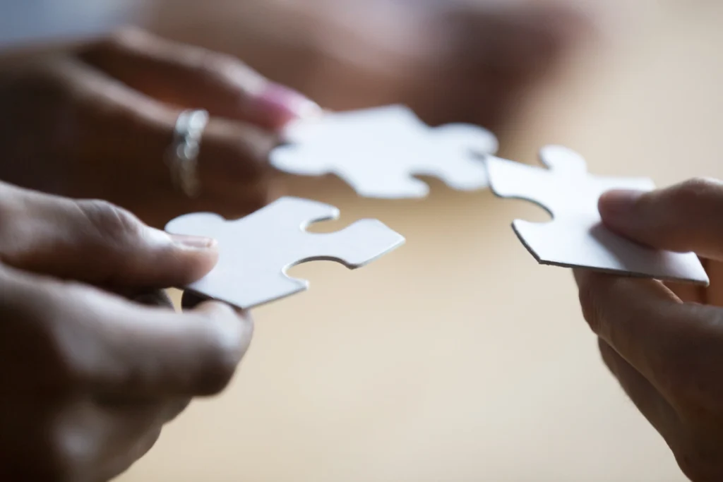 Close up hands of three teammates holding white pieces of puzzle