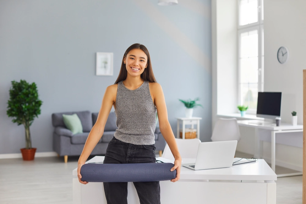 A woman holding yoga mat standing near office desk